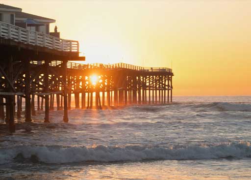 Pacific Beach shoreline at sunset with a lifeguard tower and pier in the background, representing ClearHaven Swim service area